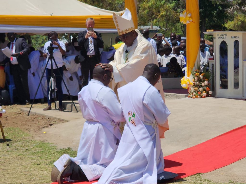 Fathers Joseph Maundu and Cavine Okello kneel before their bishop as they are ordained as priests.